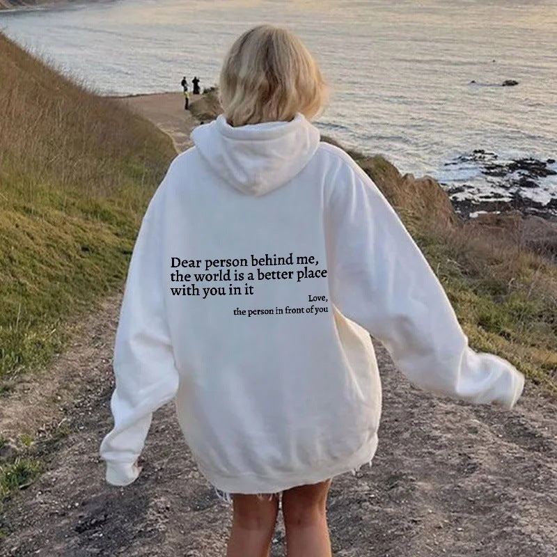 Printed hoodie with pockets featuring inspirational text on back, worn by woman outdoors near the ocean.