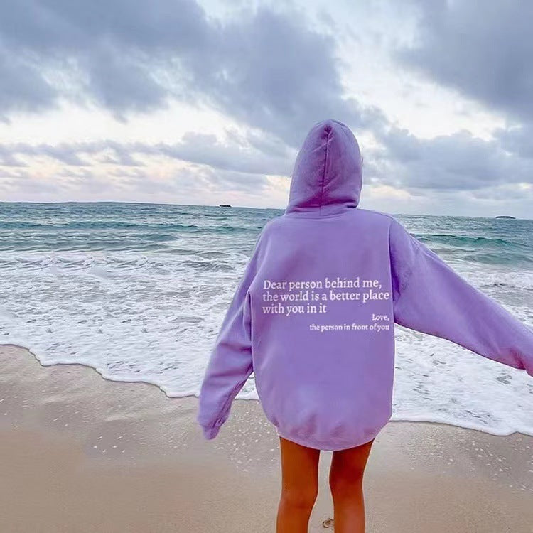 printed hoodie with pockets in lavender color, featuring a message on the back, worn by a person on the beach